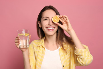 Young woman with glass of lemon water on pink background