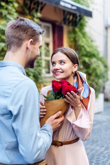young man presenting bouquet of roses to happy girlfriend on street