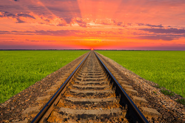 railway among green fileds leaving far to a dramatic sunset