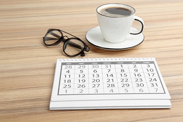 Paper calendar, cup of coffee and glasses on wooden table