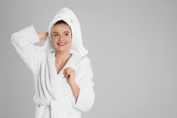 Obraz premium Beautiful young woman in bathrobe on light grey background. Space for text