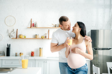 cheerful pregnant couple holding orange juice in kitchen