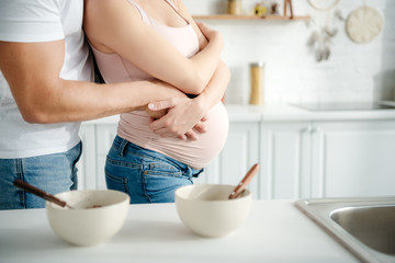 partial view of pregnant couple hugging in kitchen with cereals in bowls