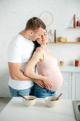 smiling pregnant couple hugging in kitchen with cereals in bowls