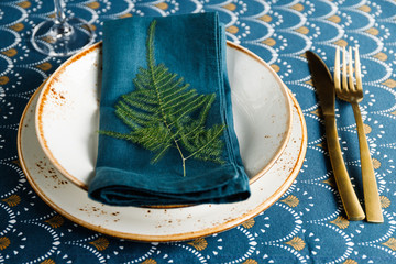 Festive table place for Christmas or New Year family dinner with Winter decor. Golden cutlery, ceramic dishes decorated with plant on a napkin.