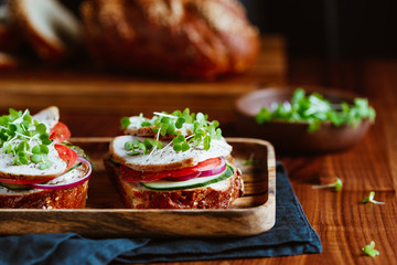 Sandwiches with turkey meat and fresh vegetables served with microgreens on a wooden plate. The concept of healthy and diet eating.