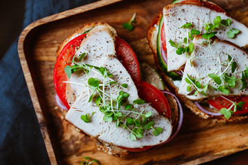 Sandwiches with turkey meat and fresh vegetables served with microgreens on a wooden plate. Top view, flat lay, macro food photography.