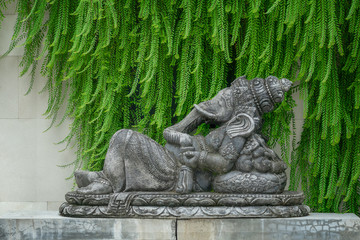 Hindu god Ganesha in lying position on a statue in front of a green and stone background.
