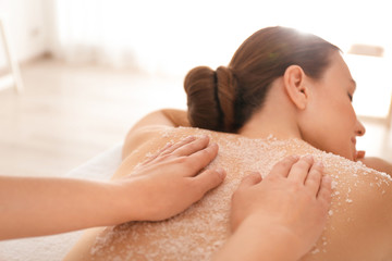 Obraz na płótnie Canvas Young woman having body scrubbing procedure with sea salt in spa salon