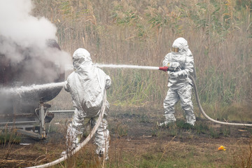 Two firefighters in protective suits works with water hose. Fighting for a fire attack