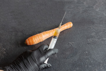 Hand of person injects chemicals into carrots, GMO fertilizers and chemicals with a syringe to...