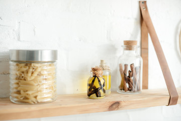 wooden shelves with spices and pasta in jars on white brick wall in kitchen