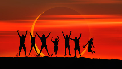 Silhouette of friends jumping on the sand dune against Solar Eclipse 