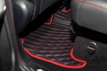 Clean black leather car floor mats with diamond  red stitching and gas pedals and brakes in the...
