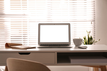 Fototapeta premium Laptop on desk near window in office. Comfortable workplace