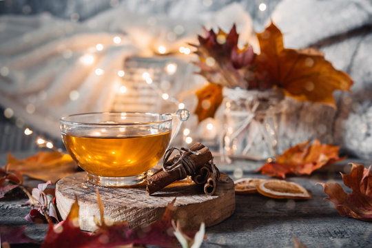 Cozy autumn or winter at home. A cup of tea, autumn casts a book a garland on a wooden table near a bed with warm plaids. Lifestyle autumn hygge lagom?concept of a holiday and autumn weekend.
