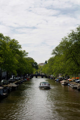 Fototapeta na wymiar View of a cruise canal tour boat, trees, parked cars and boats in Amsterdam. It is a sunny summer day.