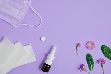 Allergy concept. Creative flat lay concept of seasonal spring and summer pollen allergy with napkins, pills, face mask, drops bottle and flowers on purple background. Top view, copy space