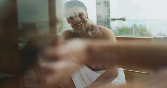An young happy couple in white bath towels is enjoying their time in sauna with the panoramic view from a window in a luxury wellness center.