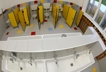 bathroom with the long sink and toilet of a school with yellow d