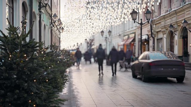 People walking along the pedestrian street in Moscow beautifully decorated to the New Year festive with Christmas trees and glittering garlands sparkling even in winter daylight.