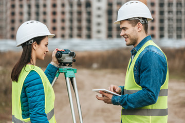 Smiling surveyors with tablet and digital level