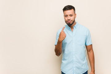 Young south-asian man pointing with finger at you as if inviting come closer.