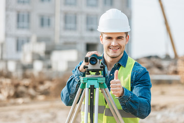 Surveyor with digital level smiling at camera and showing thumb up gesture