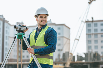 Smiling surveyor with digital level looking away on construction site