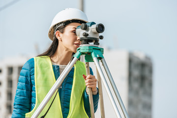 Surveyor in hardhat and high visibility jacket looking in digital level