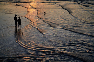 Pareja mirando al atardecer con los pies metidos en el agua de una playa