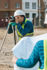 Fototapeta na wymiar Selective focus of surveyors working with digital level and blueprint