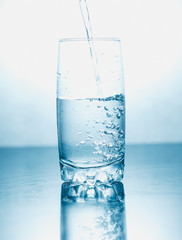 Drinking water poured into a glass isolated over blue abstract background