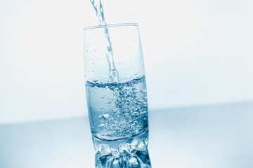 Drinking water poured into a glass isolated over blue abstract background