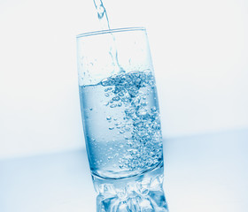 Drinking water poured into a glass isolated over blue abstract background