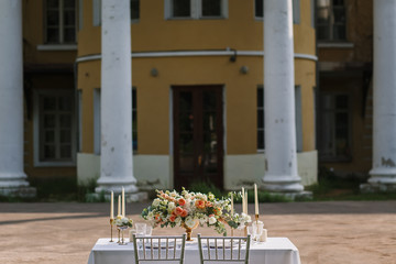 Wedding decoration table in the garden the style vintage on outdoor, floral arrangement. Decorated white table with flowers, served for two people, on the background of old building. Fine art laying.