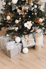 Bright silver gifts in packaging and with bows under the Christmas tree on the floor. Christmas decorations. Christmas background. Beautiful holiday decorated room 