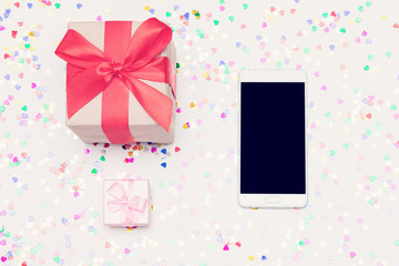 Two gift box and white smartphone, white desk with scattered scattered tinsel, close up, top view, toned