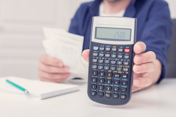 Person with bills and a calculator, man shows on the calculator the amount of 2500, male hands, cropped image, close up, toned