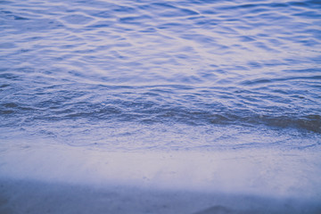 A small wave beats on the shore of the river, lake, sea. Blue shade of water. Close-up of the wave. Calm water. Background.