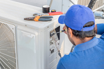 a professional electrician man is fixing a heavy duty unit of central air conditioning system by...