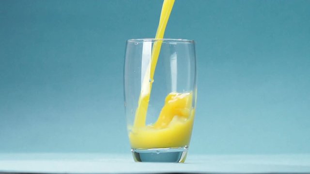 orange juice is poured into a glass on blue background