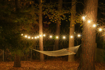 A hammock is strung up between two trees surrounded by cafe lights with starbursts; romantic...