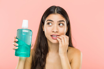 Young indian woman holding a mouthwash bottle relaxed thinking about something looking at a copy space.