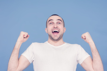 Happy man holding a smartphone and screaming: Yes! Winner!, blue background, copy space