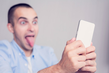 Funny man takes selfie and sticks out his tongue, focusing on a man's hand and smartphone, toned