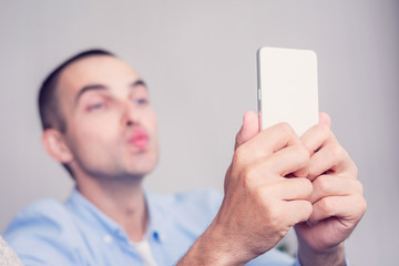 Young guy takes selfie sending air kiss, focusing on a man's hand and smartphone, toned
