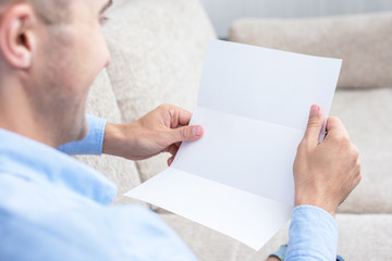 Man reading a letter at the couch, men's hands, close up, rear view, copy space, toned