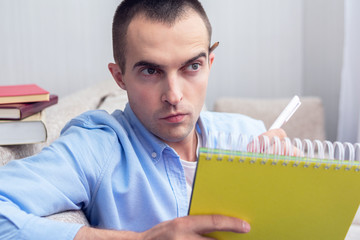 Thoughtful student with yellow notebook preparing for exams and looking at camera, close up, portrait, toned