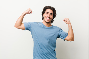 Fototapeta premium Young handsome man against a white background showing strength gesture with arms, symbol of feminine power